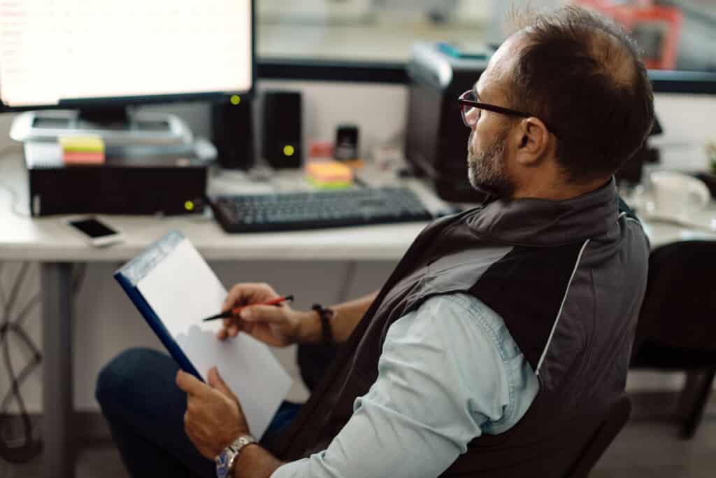 foreman using desktop pc and writing notes while working in auto